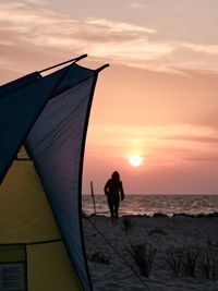 Silhouette woman walking on beach against sky during sunset