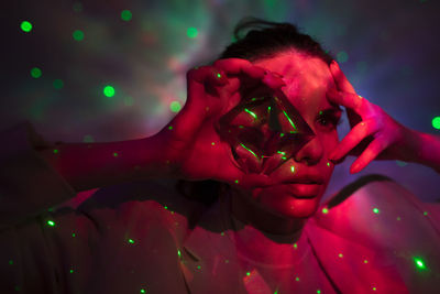 Close-up young woman looking through crystal against illuminated background