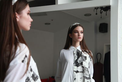 Side view of girl standing by mirror at home