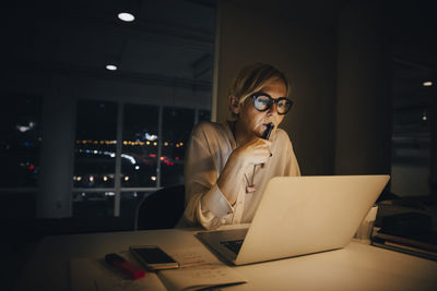 Thoughtful businesswoman looking at laptop while working late in creative office