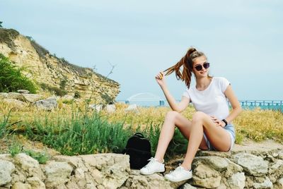 Full length of young woman sitting on land against sky