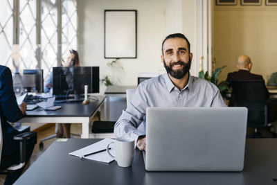 Confident hipster entrepreneur working on laptop at desk in office