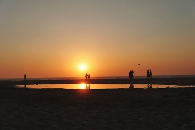 Silhouette people on beach against sky during sunset