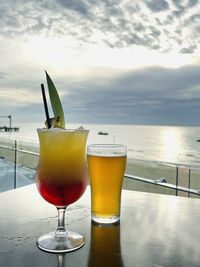 Beer glass on table by sea against sky