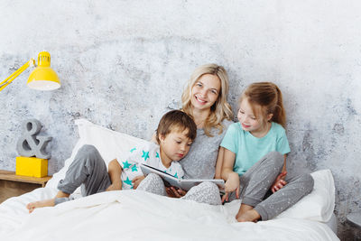 Mother and children reading book on bed at home