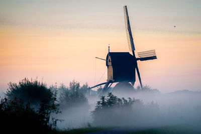 Windmill on landscape against sky during sunset