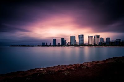 Sea and buildings against cloudy sky during sunset
