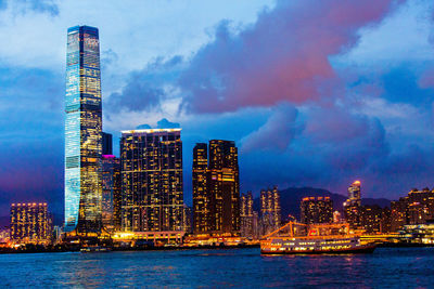 Illuminated city by sea against sky