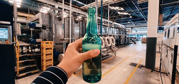 Midsection of person holding glass of machine in factory