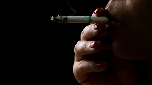 Close-up of woman smoking cigarette against black background