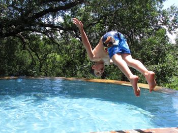 Full length of shirtless boy jumping into swimming pool against trees