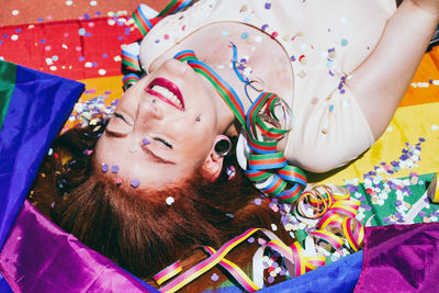 Young woman lying down on rainbow flag during sunny day