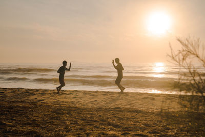 Silhouette two man run on beach with sunrise and sea background