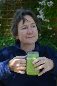 Thoughtful mature woman having healthy drink while sitting at yard