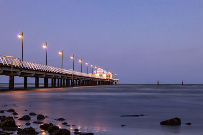 Illuminated bridge over sea against sky at dusk