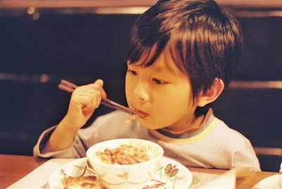 Cute boy eating food with chopsticks at home