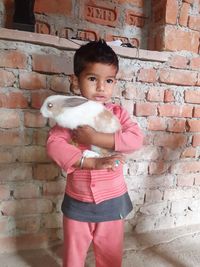 Thoughtful boy holding rabbit while standing against brick wall