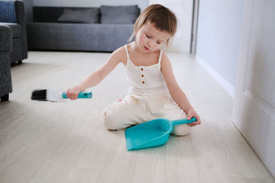 Cute european child with blue scoop for garbage and brush for sweeping floor helps to clean,