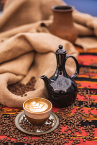 Cappuccino in a ceramic cup with flower or leaves drawn on the foam, teapot and roasted coffee beans
