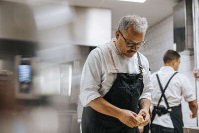 Mature male chef with eyeglasses kneading dough in restaurant kitchen