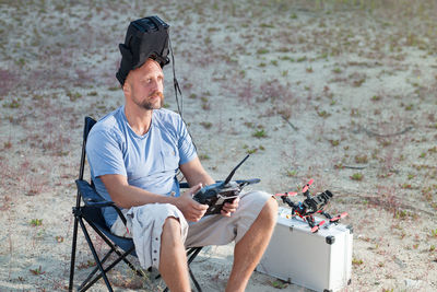 Man sitting with drone and remote control on field