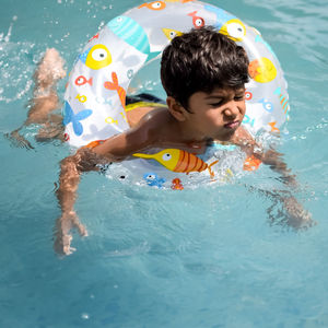 Happy indian boy swimming in a pool, kid wearing swimming costume along with air tube during day