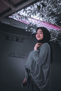 Portrait of young woman standing against wall