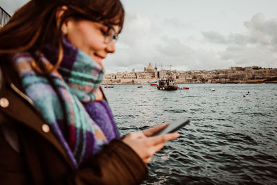 Young woman using smart phone by sea against sky