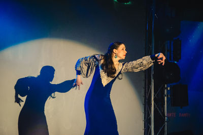 Young woman standing against wall at night