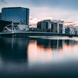 Bridge over river by buildings against sky during sunset