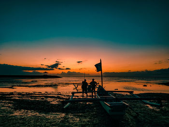 Silhouette people sitting on beach against sky during sunset