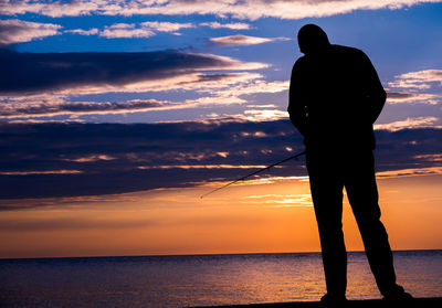 Silhouette man standing by sea against sky during sunset