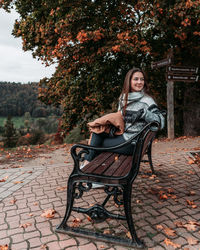 Portrait of smiling young woman sitting on tree during autumn
