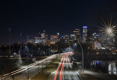 Light trails on road amidst buildings against sky at night