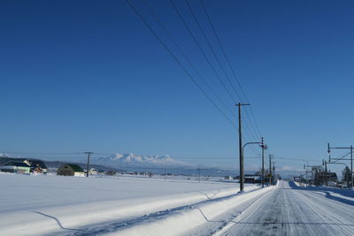 Road by snow covered landscape against clear blue sky