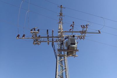 Low angle view of electricity pylon against clear blue sky