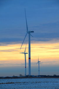 Wind turbines against sky during sunset
