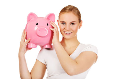 Portrait of smiling young woman holding piggy bank against white background