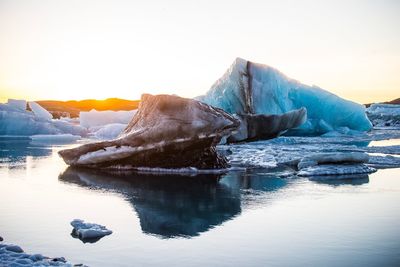 Icebergs in sea against clear sky during sunset