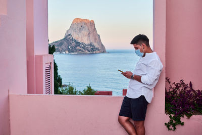 Man standing on mobile phone by sea against sky