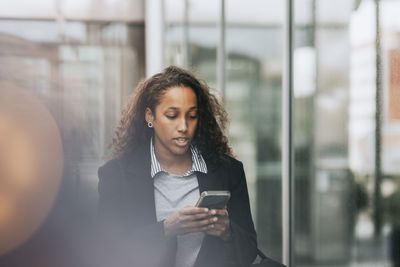 Young female business professional using smart phone near building