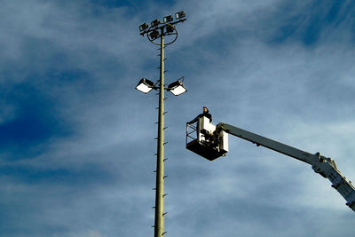 Maintenance engineer on cherry picker reaching towards floodlight