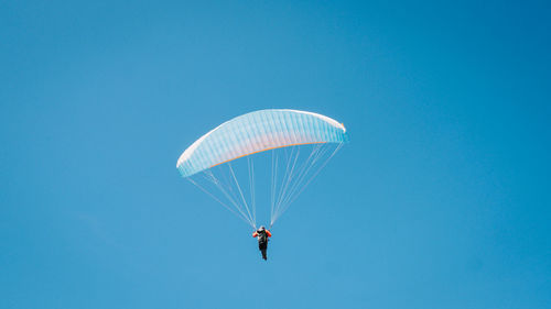 Low angle view of man paragliding against clear blue sky