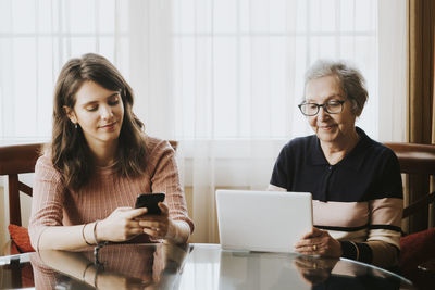 Granddaughter using mobile and grandmother using tablet