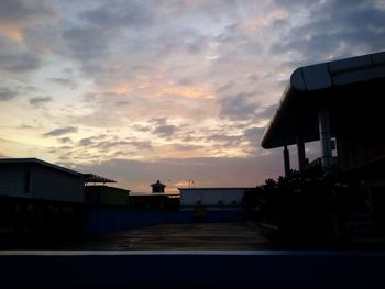 Silhouette houses by sea against dramatic sky