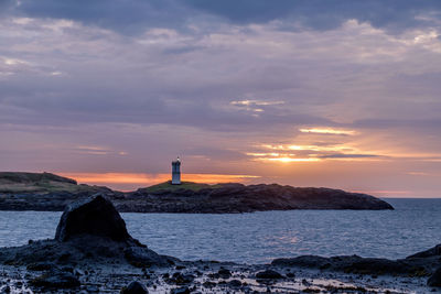 Lighthouse by sea against sky during sunset