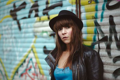 Portrait of woman wearing hat against graffiti shutter in city