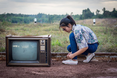 Woman wearing shoe by old television set on field