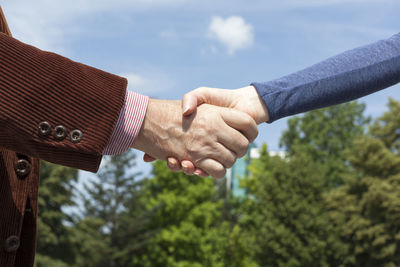 Close-up of couple holding hands against sky