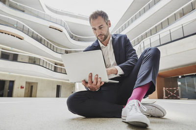 Businesssman sitting on floor in office building using laptop